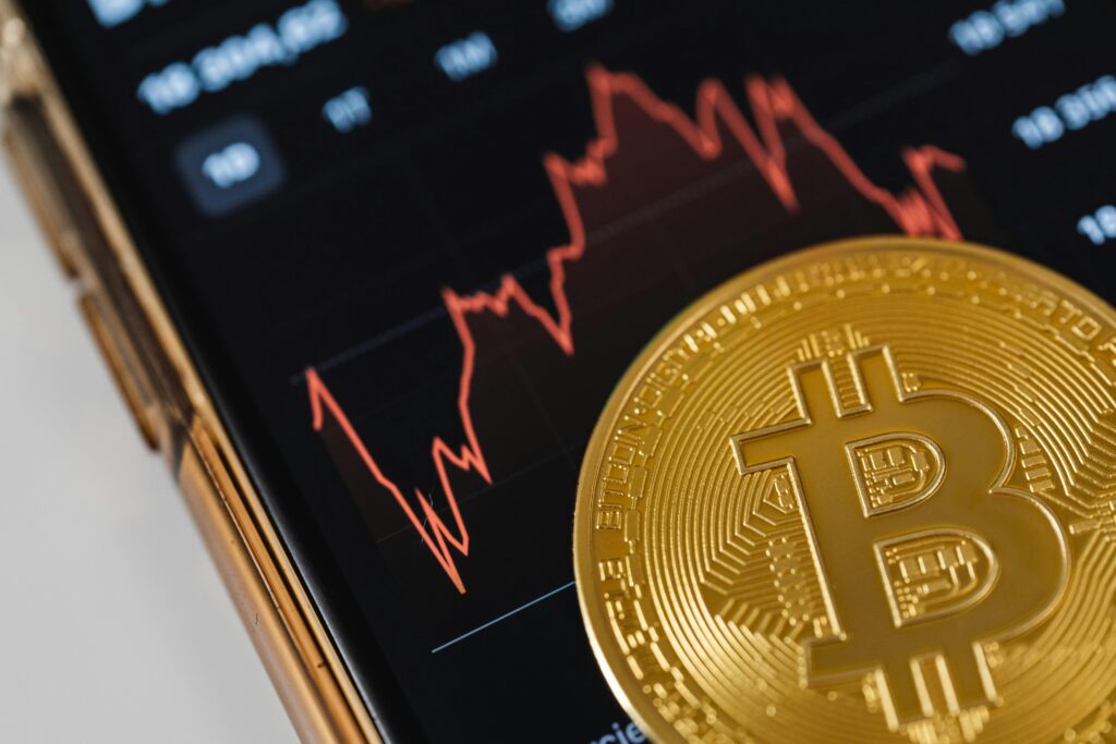 A gold Bitcoin coin on a smartphone displaying a fluctuating stock market chart.