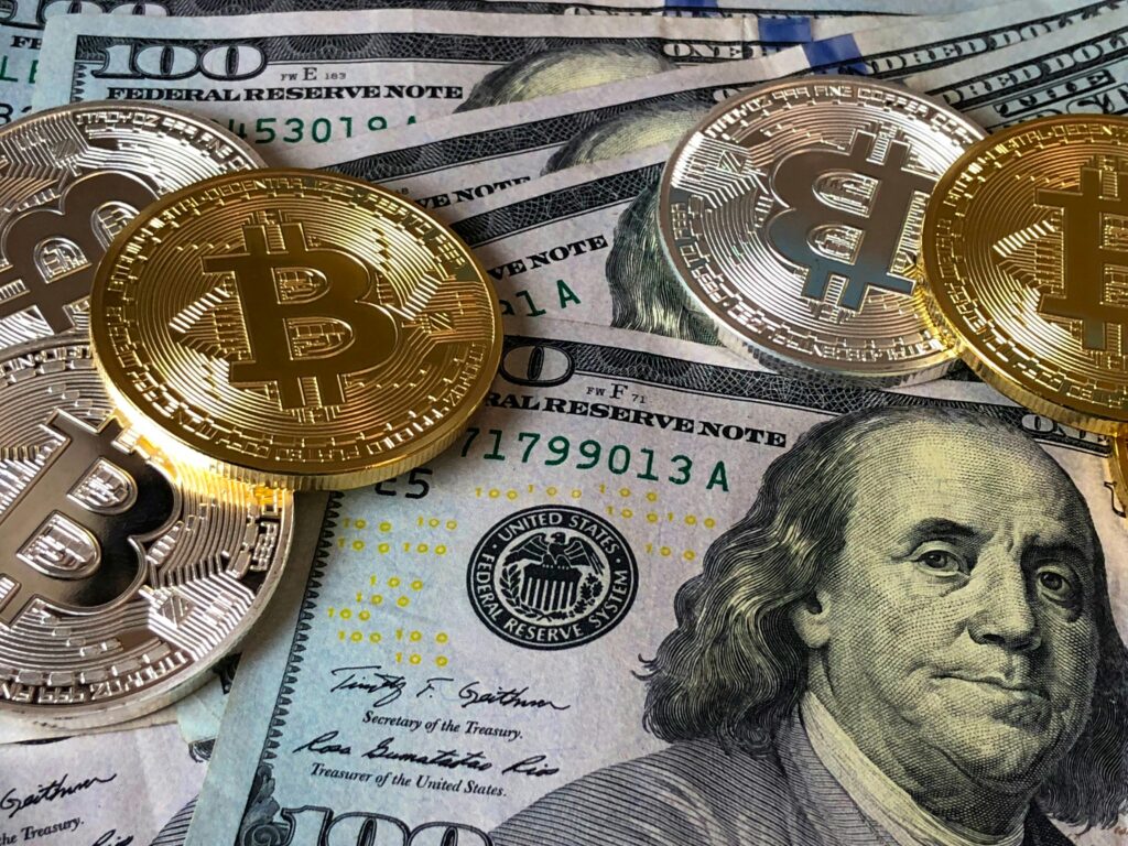 A close-up photo depicting Bitcoin coins on top of US dollar bills, symbolizing finance and cryptocurrency.