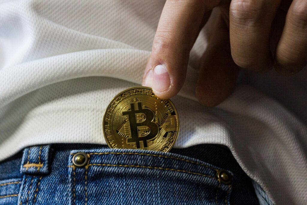 Close-up of hand putting Bitcoin in jeans pocket symbolizing cryptocurrency savings.